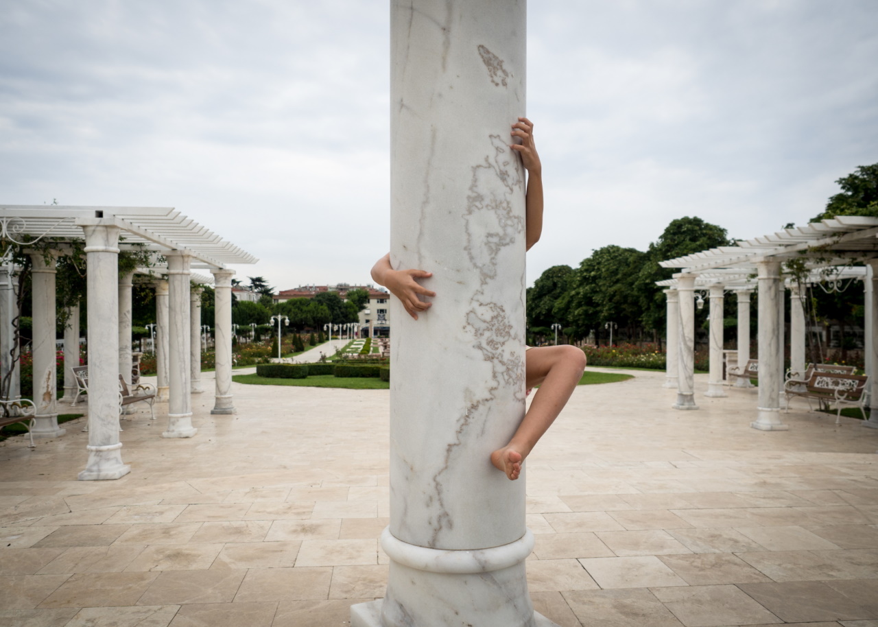 Girl hiding behind a column with two hands and a leg showing